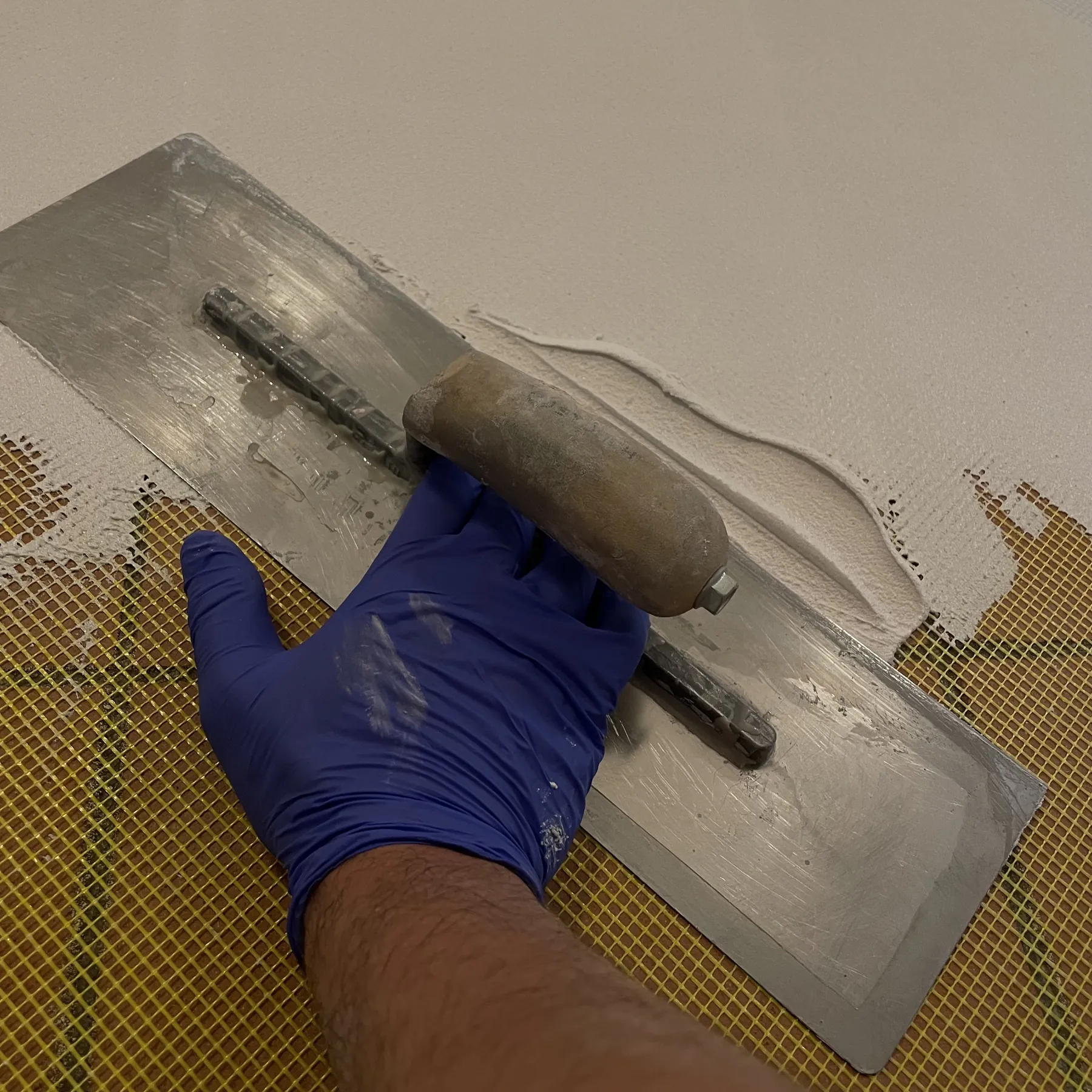 Mano con guanto che stende il materiale con un frattazzo su una rete di armatura
