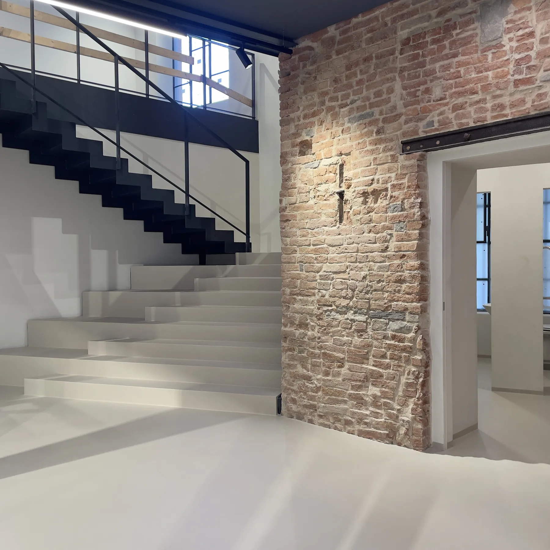 Scala e pavimento chiari in resina continua accanto a una parete in mattoni a vista