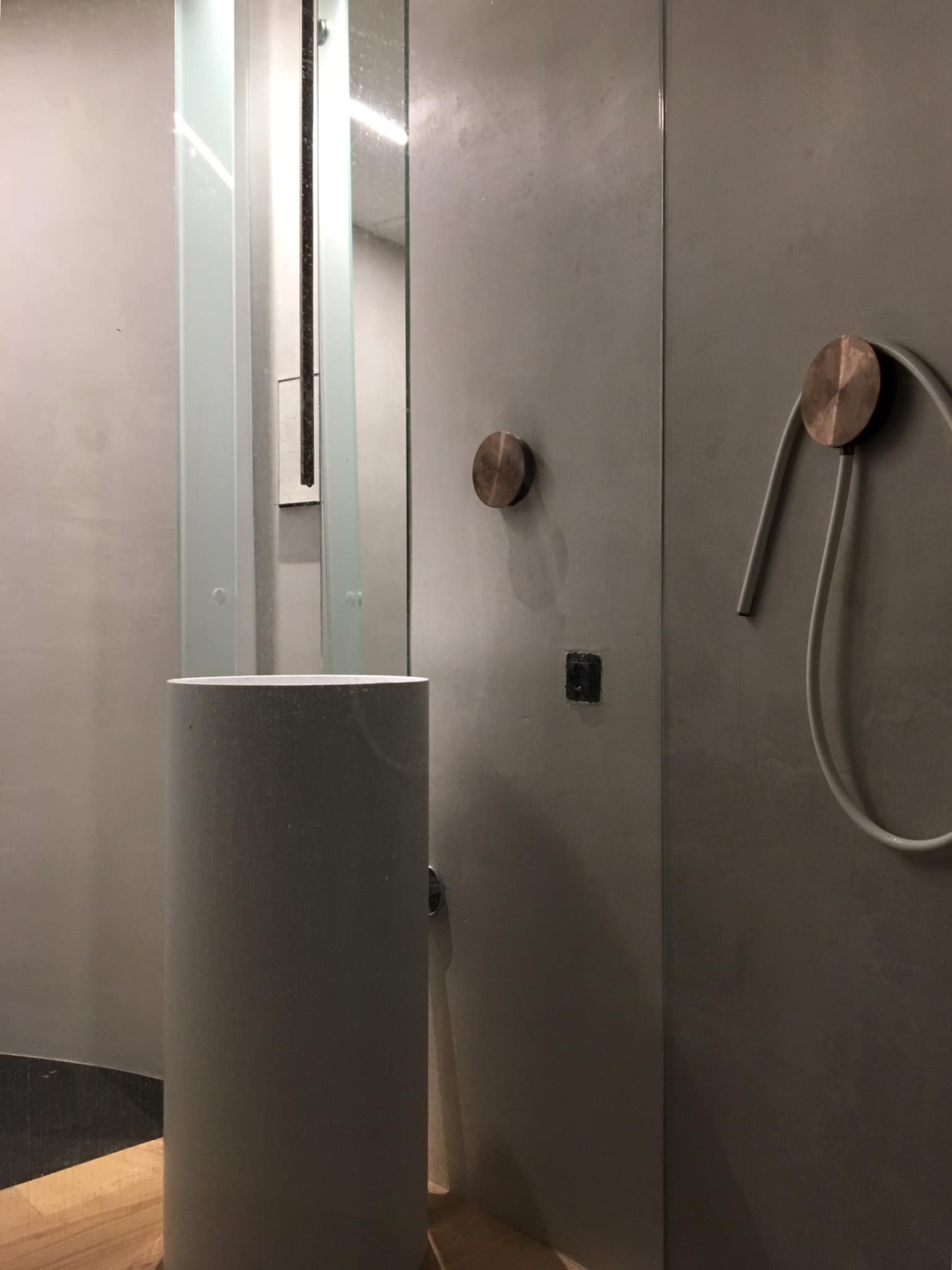 Bagno con lavabo a colonna, parete continua grigia e rubinetteria ramata