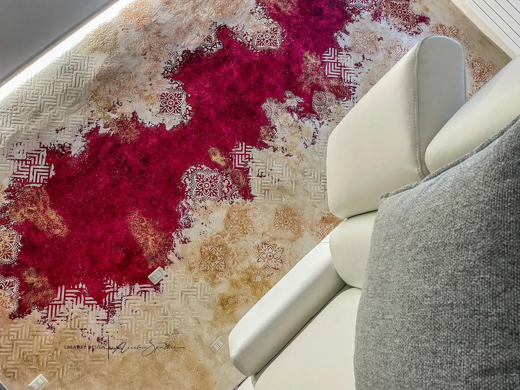 Parete decorativa con macchie materiche rosso porpora e texture a rilievo dietro un divano bianco