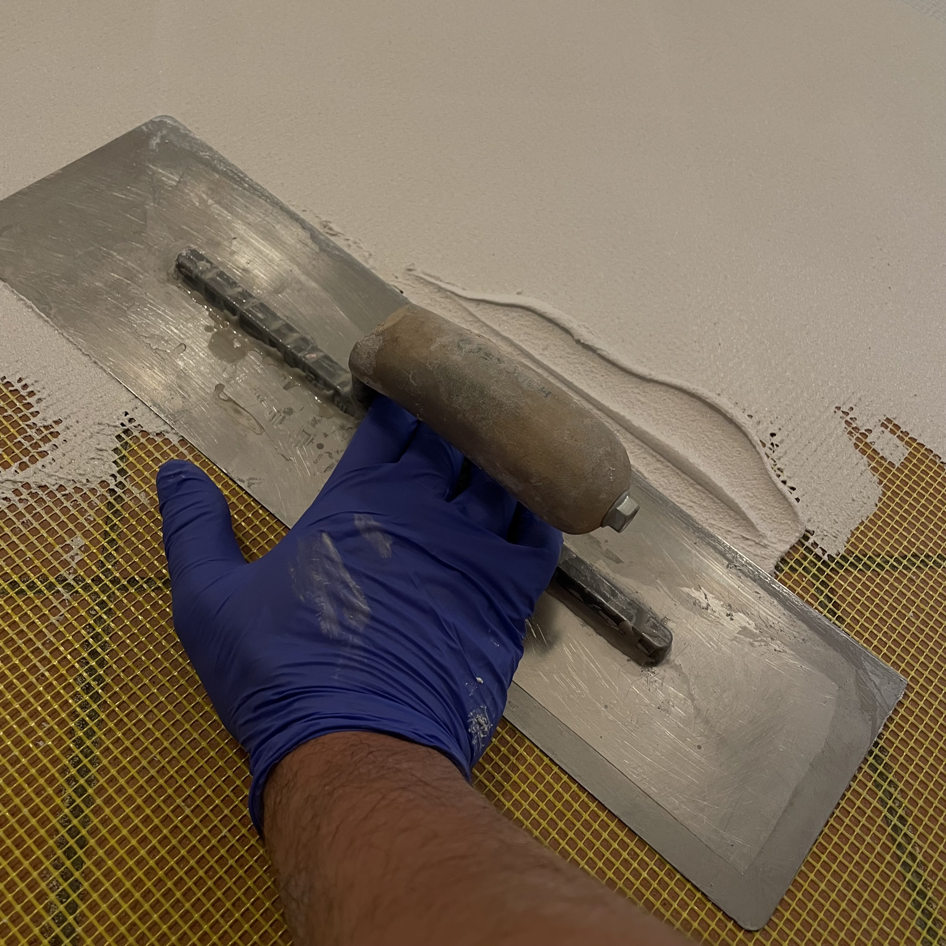 Mano guantata e frattazzo metallico sulla materia, con rete visibile