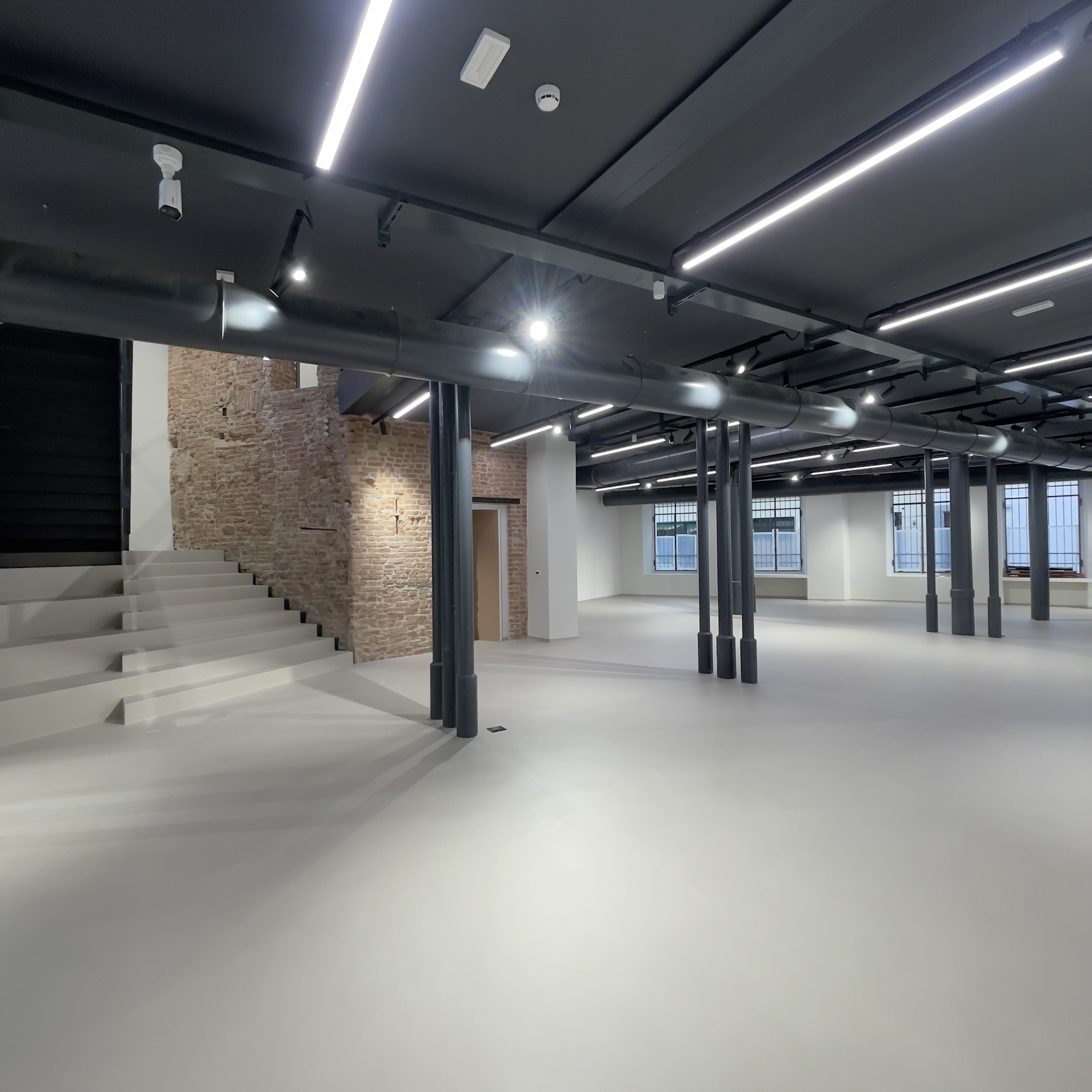 Grande ambiente con pavimento continuo, colonne e scala
