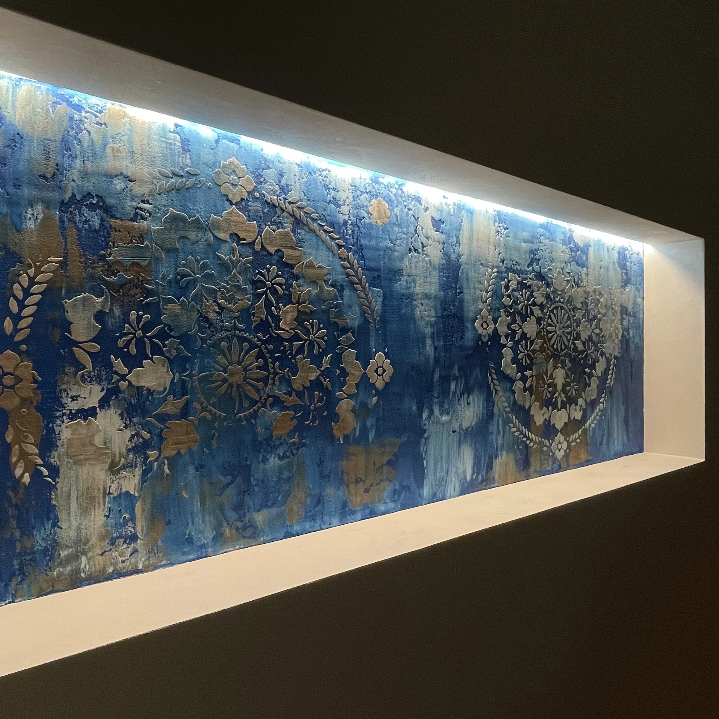 Pannello decorativo blu e oro con motivi ornamentali svelati da una luce radente
