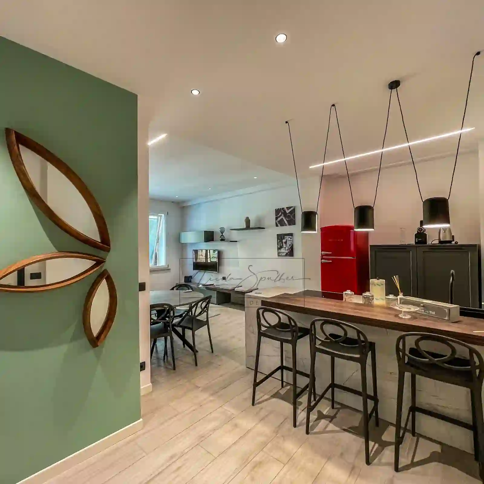 Zona pranzo con parete verde, specchio ovale e cucina sullo sfondo