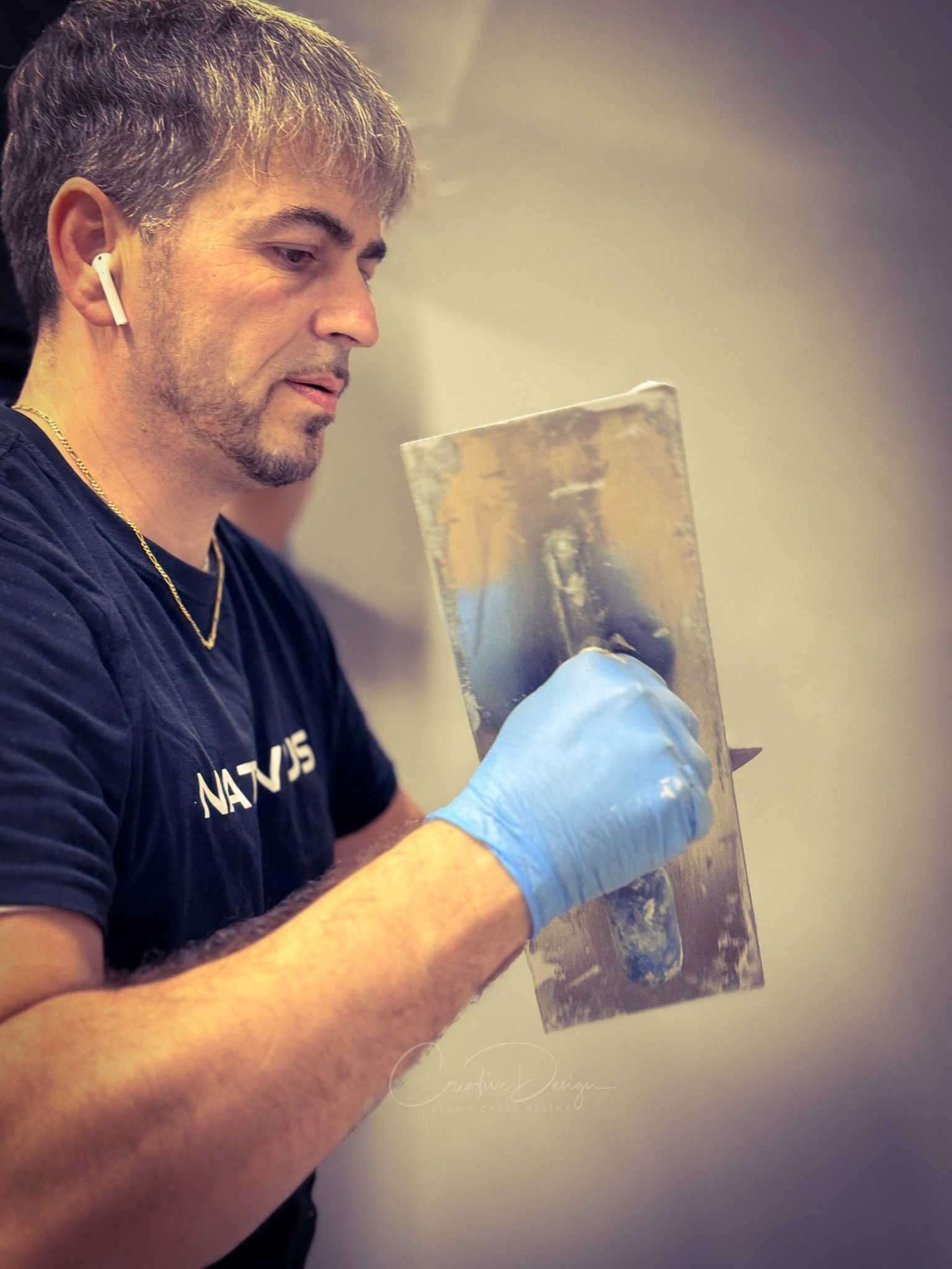 Artigiano con guanto blu e spatola metallica davanti a una parete